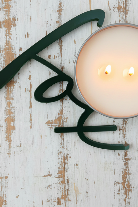 A white candle placed on a old whitewashed surface, with the dual wicks burning and wax visible.