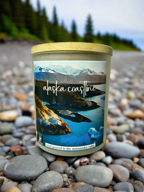 Candle with 'Alaska Coastline' label on pebbles