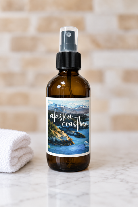 Brown spray bottle with 'Alaska Coastline' label on a marble surface with a plant and towel in the background.