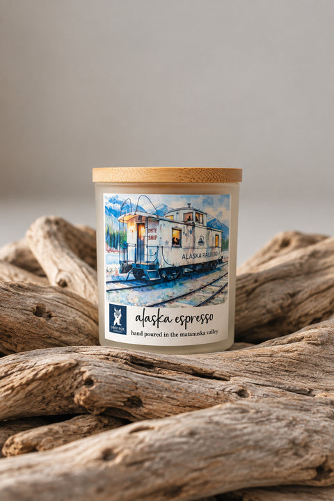 Alaska Espresso coconut wax candle in white frosted vessel with bamboo lid, styled on a warm wooden dining table next to a steaming coffee cup and eucalyptus sprig, Grey Fox Candles