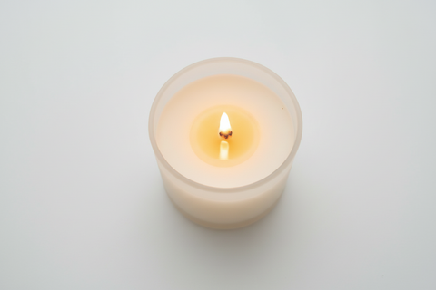 A lit cream-colored candle in a frosted glass holder, photographed from directly above on a clean, light gray background.