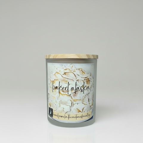 Candle labeled 'Baked Alaska' on a wooden surface with a kitchen background