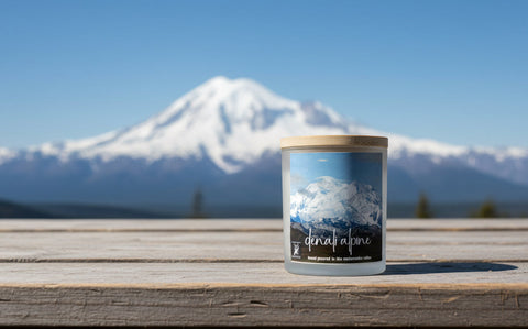 Candle with mountain view packaging on a wooden surface with a mountain in the background