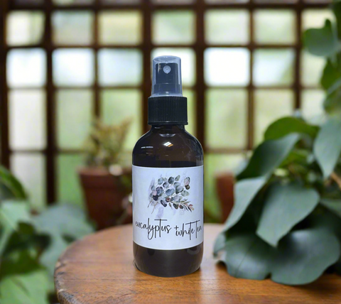 Bottle of eucalyptus and white tea spray on a wooden surface with plants in the background
