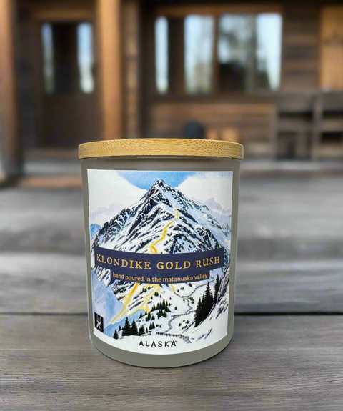 Candle with a mountain label titled 'Klondike gold rush'on a wooden surface
