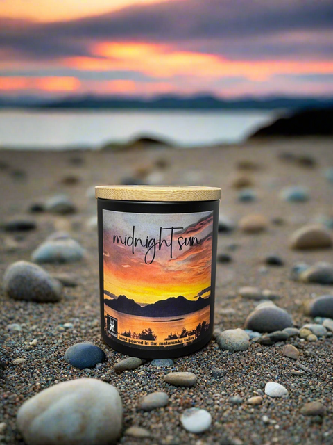 Candle labeled 'midnight sun' on a beach with a sunset in the background