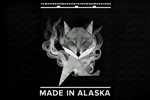 A black square graphic featuring a stylized low-poly fox head made of gray and white geometric shapes with smoke-like white swirls around it. White text at the top and bottom reads 'MADE IN ALASKA'.