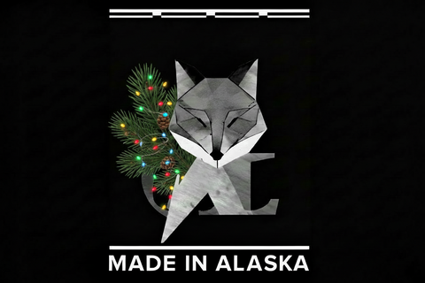 A black graphic print featuring a stylized geometric fox head in gray and white, partially overlaid with a green Christmas tree branch decorated with multicolored lights. The text 'MADE IN ALASKA' appears in white at the bottom.