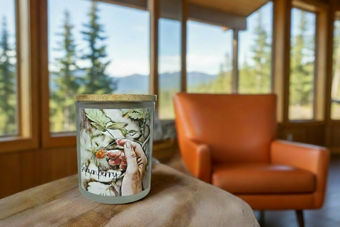Candle with salmonberry watercolor decorative label on a wooden surface in front of a stone fireplace, by grey fox candles