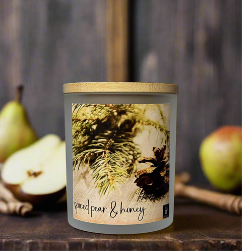 Candle with 'spiced pear & honey' label on a wooden surface with pears in the background