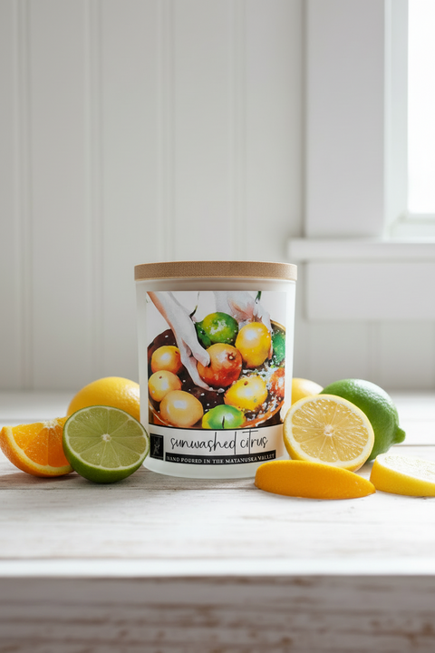 Jar of sun-dried citrus on a wooden surface with lemons and limes and a candle named 'sunwashed citrus'