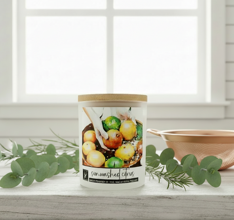 Candle with a fruit illustration on a wooden surface with greenery