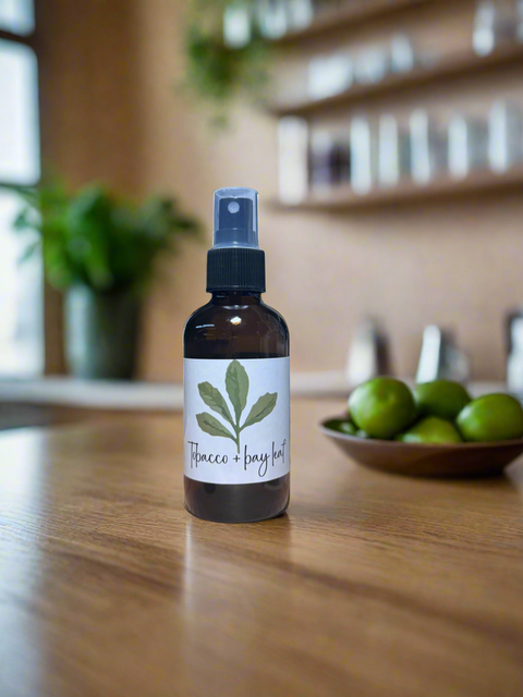 Bottle of Tobacco Bay Leaf spray on a wood surface with a plant in the background