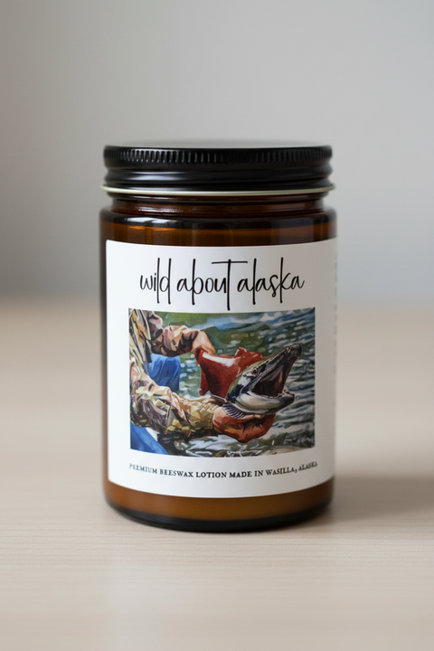 'wild about alaska' premium beeswax lotion, featuring a central illustration of a person catching a salmon over water, with ingredients listed on the right and a 'Made in Alaska' seal on the left, all on a white background.
