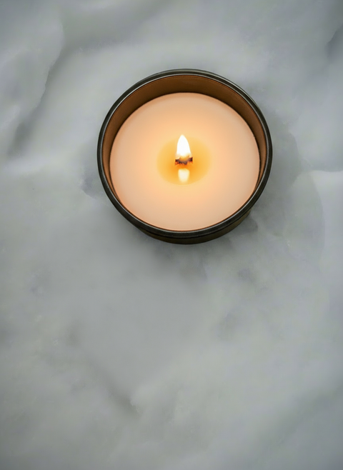 Candle in a matte black glass container on snow, wood wick burning