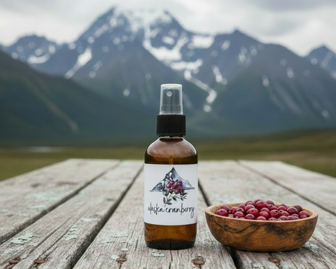 Bottle of Alaska cranberry spray on a wooden surface with a bowl of berries and mountains in the background
