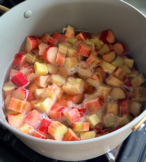 Chopped rhubarb with red, pink, and pale yellow stalks simmering in water inside a light gray pot on a stovetop.