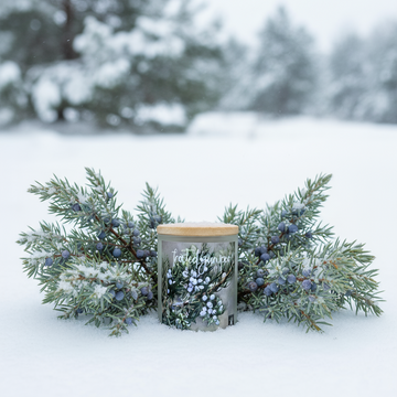 Decorative candle with Christmas tree design on a table in a cozy room with stone fireplace and Christmas tree.