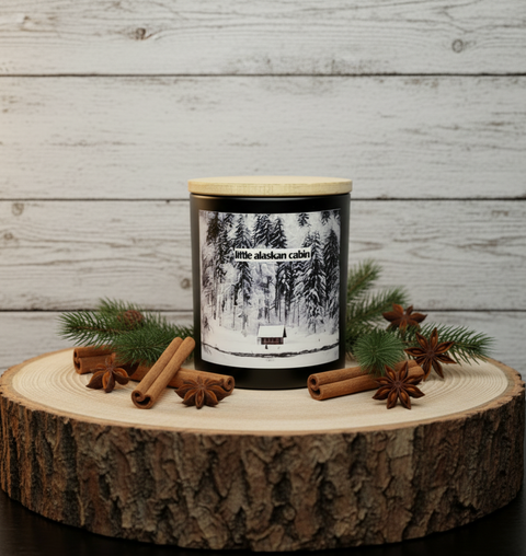 Candle with a forest design label on a wooden platform with cinnamon sticks and pine branches against a wooden background.
