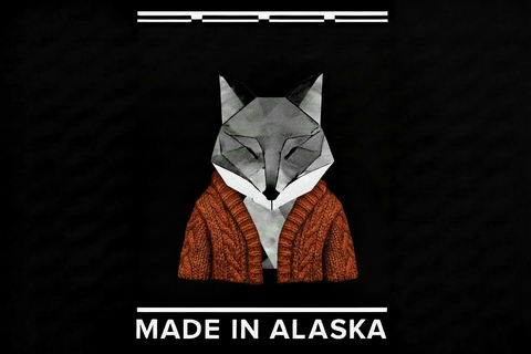 A stylized fox head made of geometric polygon shapes wearing a gold cable-knit sweater, centered on a black background with the text 'MADE IN ALASKA' below and white horizontal line accents at the top and bottom.