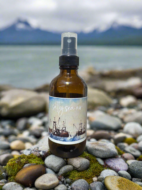 Brown spray bottle with a label on a pebbly beach with alaska mountains in the background