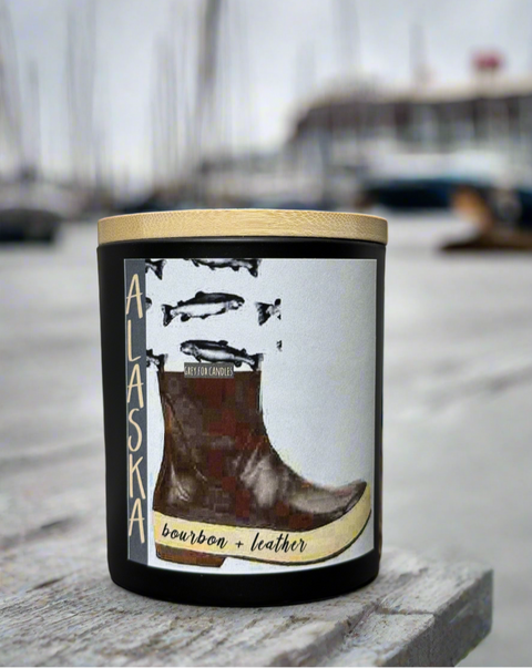 bourbon and leather Alaska water boot candle on a pier, blurred images of sailboats in the background