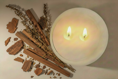 Two lit candles with cinnamon sticks and dried herbs on a neutral background