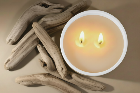 Two lit candle wick flames on a bed of driftwood with a neutral background