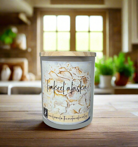 Candle labeled 'Baked Alaska' on a wooden surface with a kitchen background
