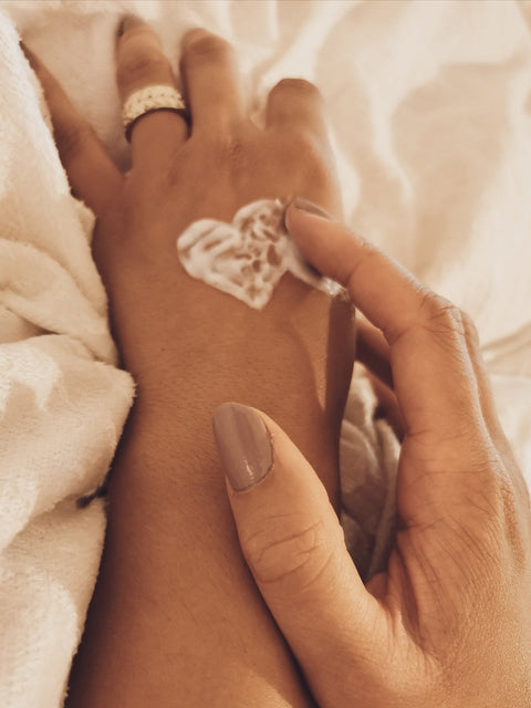 Close-up of beeswax lotion applied in a heart shape on the back of a hand, being gently massaged in.
