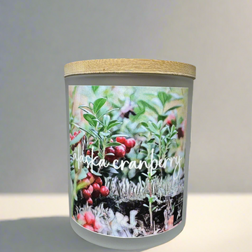 Candle with 'Alaska Cranberry' label and natural elements on a gray background