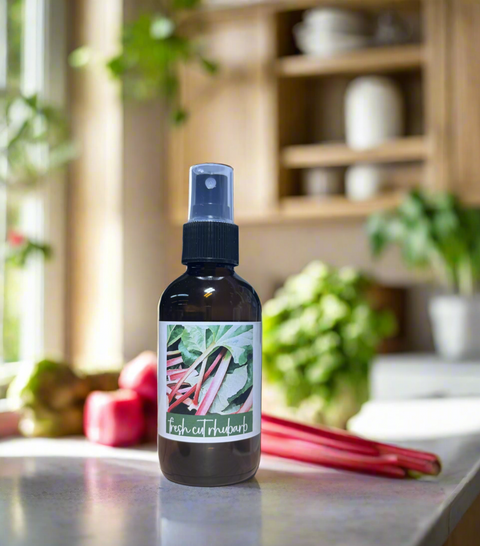 Bottle of fresh-cut rhubarb linen spray on a kitchen counter with rhubarb stalks and a blurred background.
