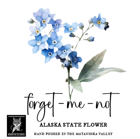 Alaska state flower forget-me-not water color art lable with blue and white forget me not flowers, green leaves, and black text reading 'forget-me-not', 'ALASKA STATE FLOWER', and 'HAND POURED IN THE MATANUSKA VALLEY'. A small 'Made in Alaska' logo appears in the lower left on a white background.