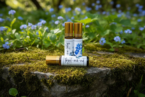 roll on perfume in an 10ml amber glass vial, shown outdoors on moss and stone with real forget-me-not flowers. fragrance is forget me not, made in alaska by grey fox candles.
