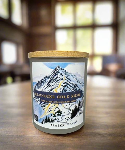 Candle with mountain design and 'Klondike Gold Rush' text on a wooden surface