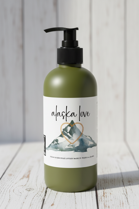 Alaska Love premium beeswax lotion label featuring a watercolor mountain with a heart-shaped gold border outline and a fox logo on a white shiplap background.