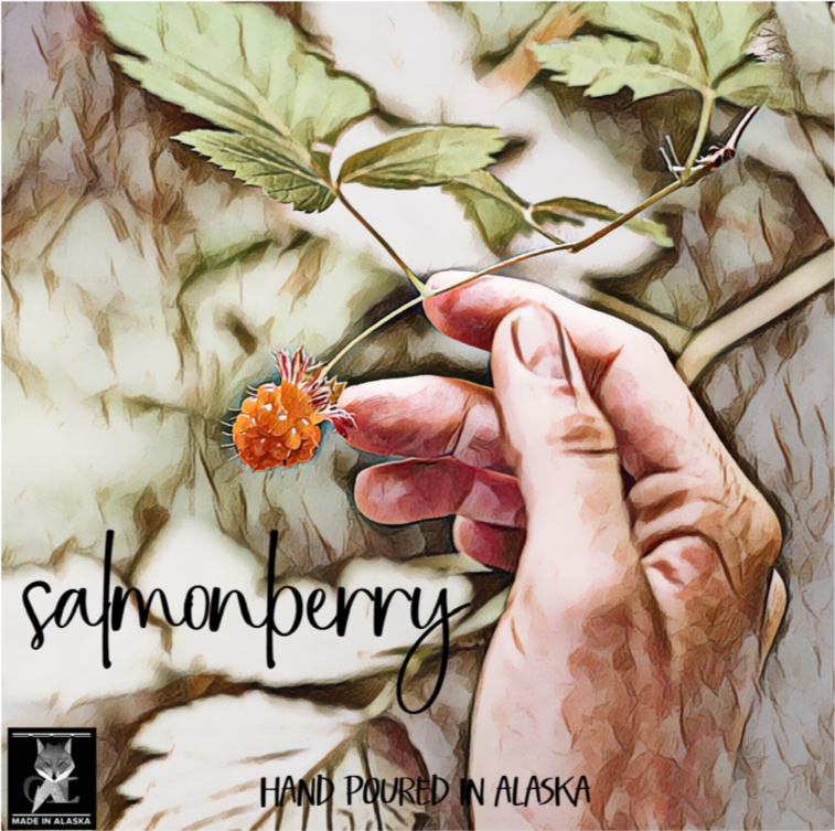 Hand holding a salmonberry with leaves on a textured background, labeled 'salmonberry' and 'hand poured in Alaska'.