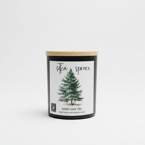 Candle labeled 'Silka Spruce' and 'alaska state tree' in a white studio setting 