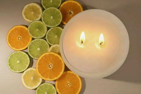 Candle with two flames surrounded by sliced oranges and limes on a neutral background