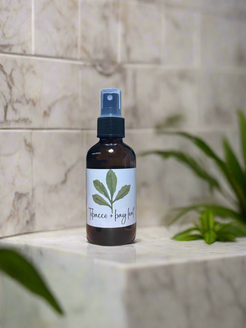 Bottle of Tobacco Bay Leaf spray on a marble surface with a plant in the background