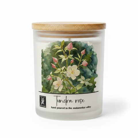 A frosted glass jar candle with a light bamboo wood lid, featuring a watercolor label of a 'Tundra Rose' with white flowers and green leaves on a white background.