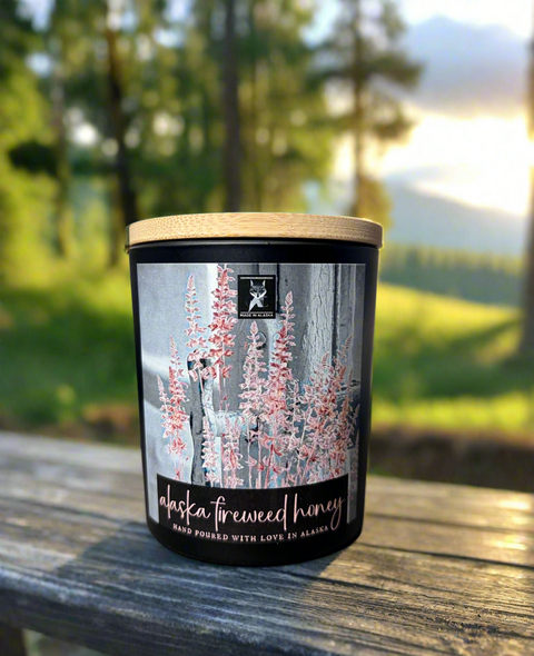 Candle with a label featuring fireweed flowers on a wooden surface with a natural background