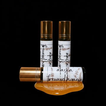 Three perfume roll on bottles labeled 'Alaskan Fireweed Honey' on a black background
