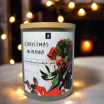 Candle with a label titled 'Christmas in Alaska' against a softly blurred background with lights.
