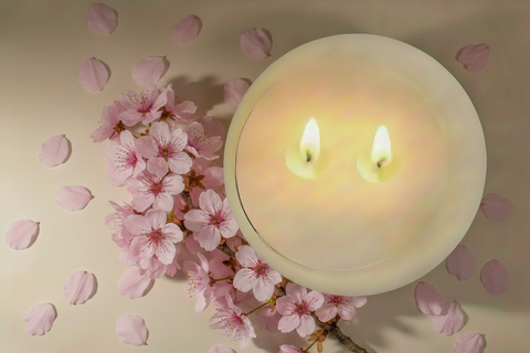 Two lit candles with a bundle of cherry blossom on a neutral background