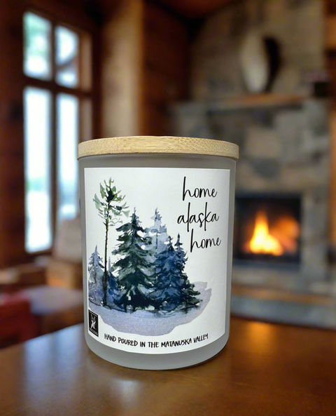 Candle with 'home alaska home' label in front of a fireplace