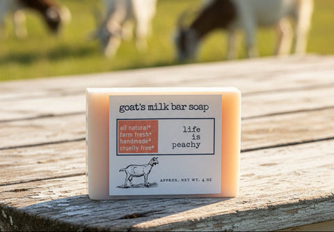 Goats' milk bar soap on a wood farmhouse table with sheep in the background