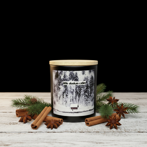 Candle with a forest design label on a wooden surface with cinnamon sticks and pine branches.