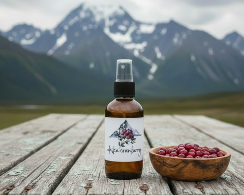 Bottle of Alaska cranberry spray on a wooden surface with a bowl of berries and mountains in the background