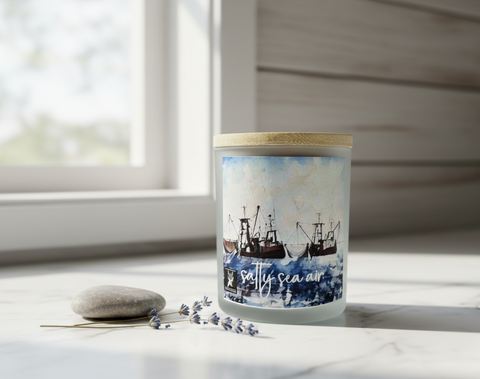 Candle with a label featuring a ship design and 'salty sea air' text, placed on a light surface.
